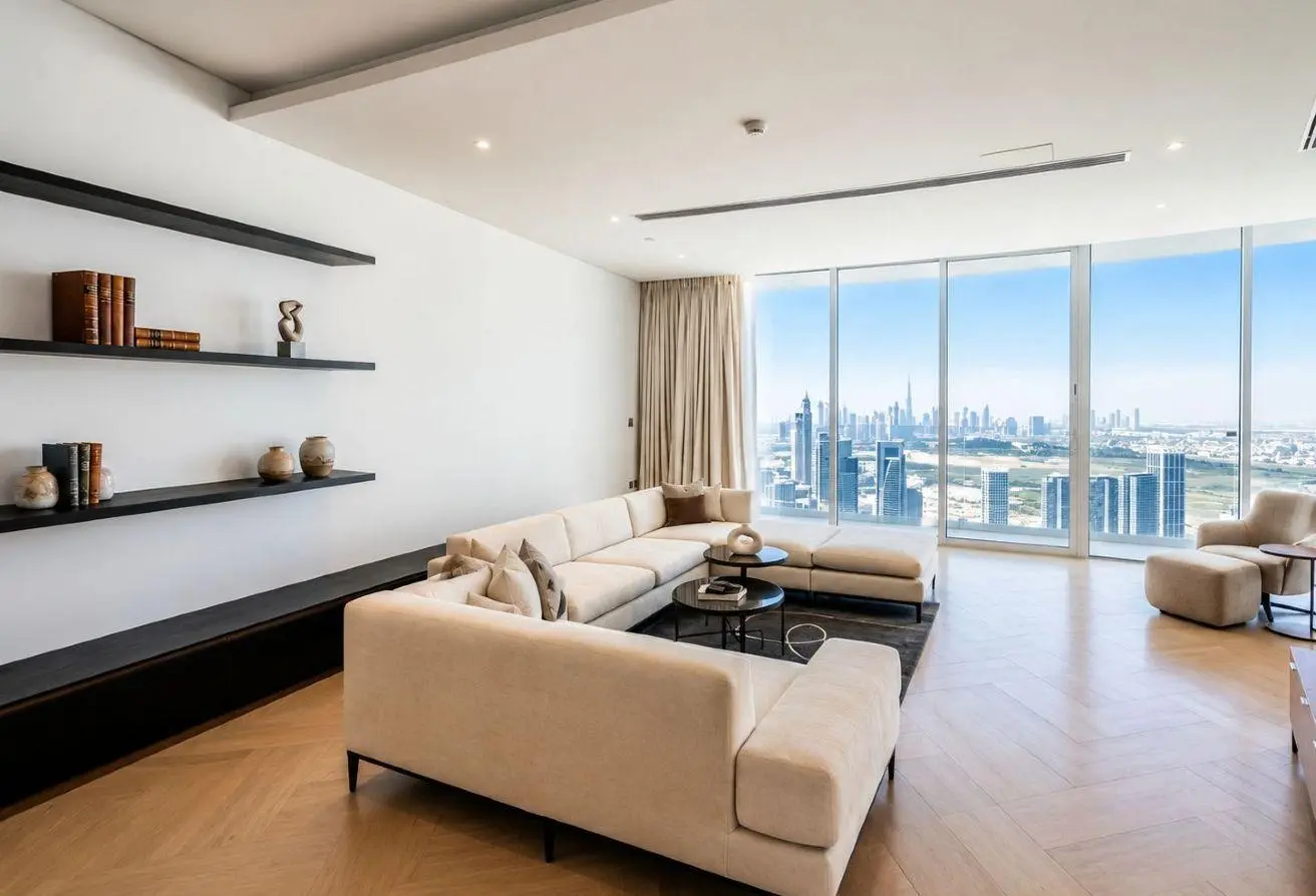 Bright, modern living room with beige sectional sofa, black shelves, and a city skyline view through floor-to-ceiling windows.