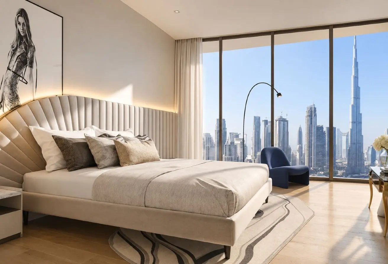 Luxurious bedroom with a beige upholstered bed, multiple pillows, and a curved headboard set against a large window overlooking a city skyline.