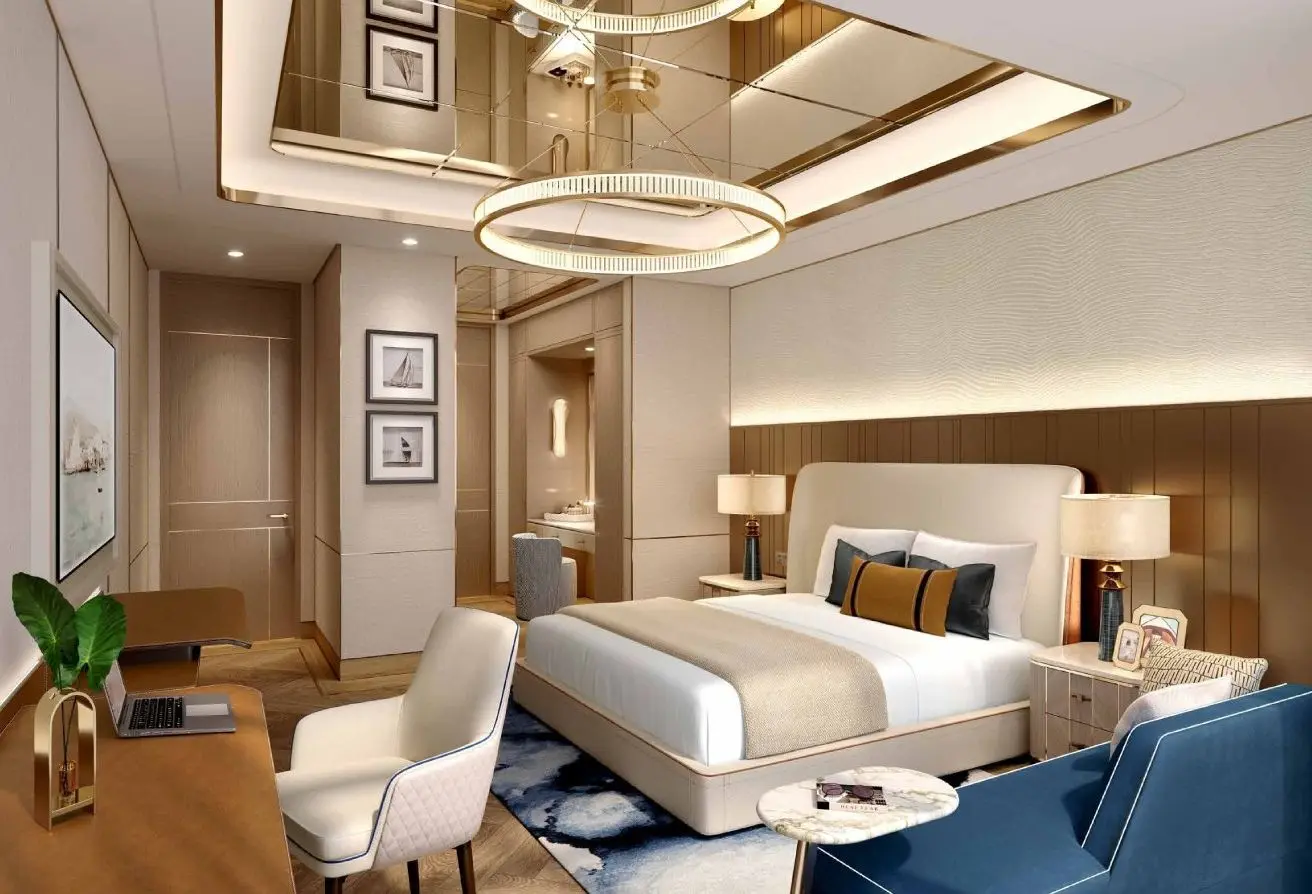 Luxurious hotel bedroom with a king bed, beige headboard, gold accents, and a blue chair under warm lighting.