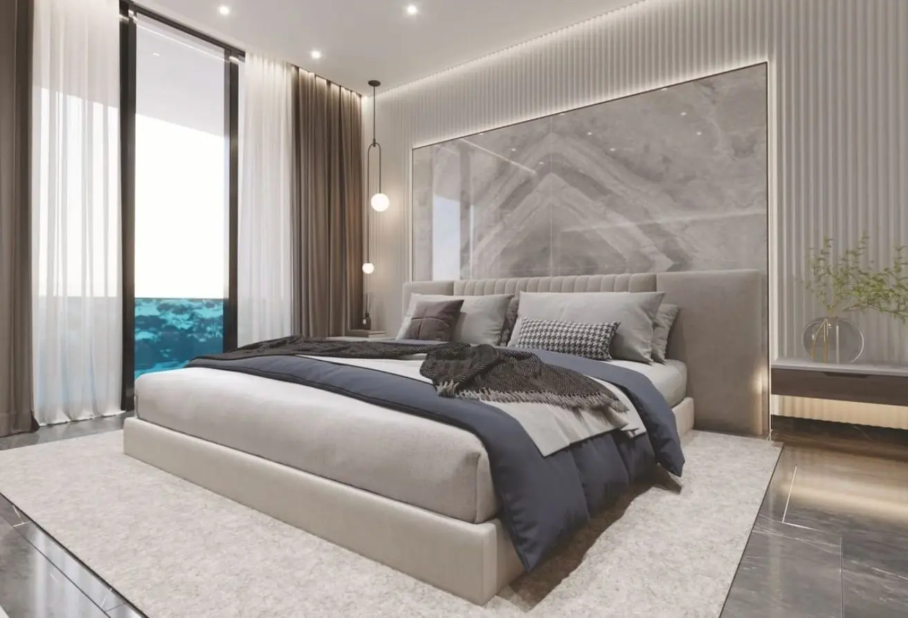 Luxurious modern bedroom with a low beige platform bed, tufted headboard, marble wall panel, and sheer-curtained windows. A balcony view is visible outside.