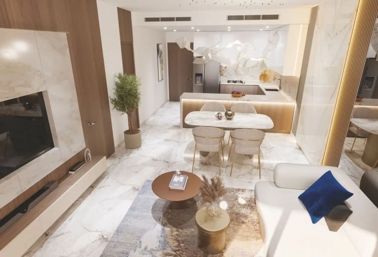 Open-plan living area with marble floors, white sofa and blue pillow facing a round coffee table and rug, adjacent to a marble-finished kitchen island.