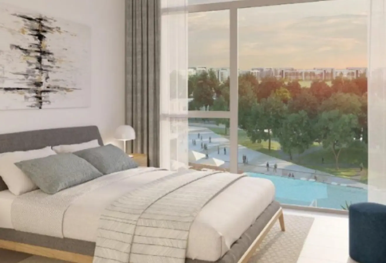 Modern bedroom with a low gray bed, white bedding and light-gray pillows; large windows reveal a park, lake, and distant buildings outside.