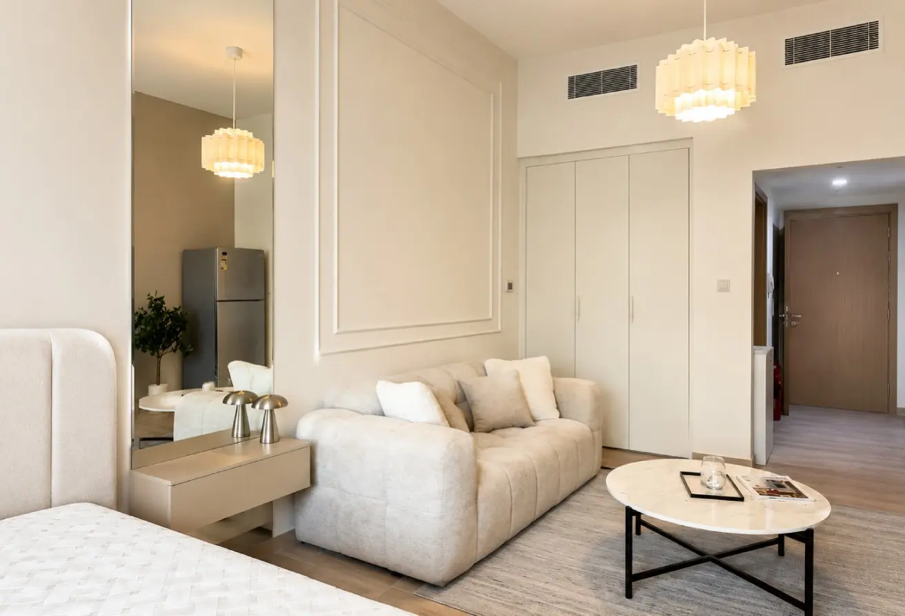 Bright living room with a cream sofa, white cushions, a round marble coffee table, and a large wall mirror on the left.