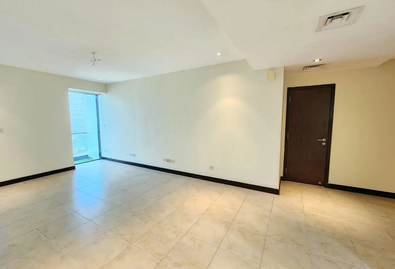 Empty living room with white walls, tiled floor, a dark wooden door, and glass balcony door on the left.