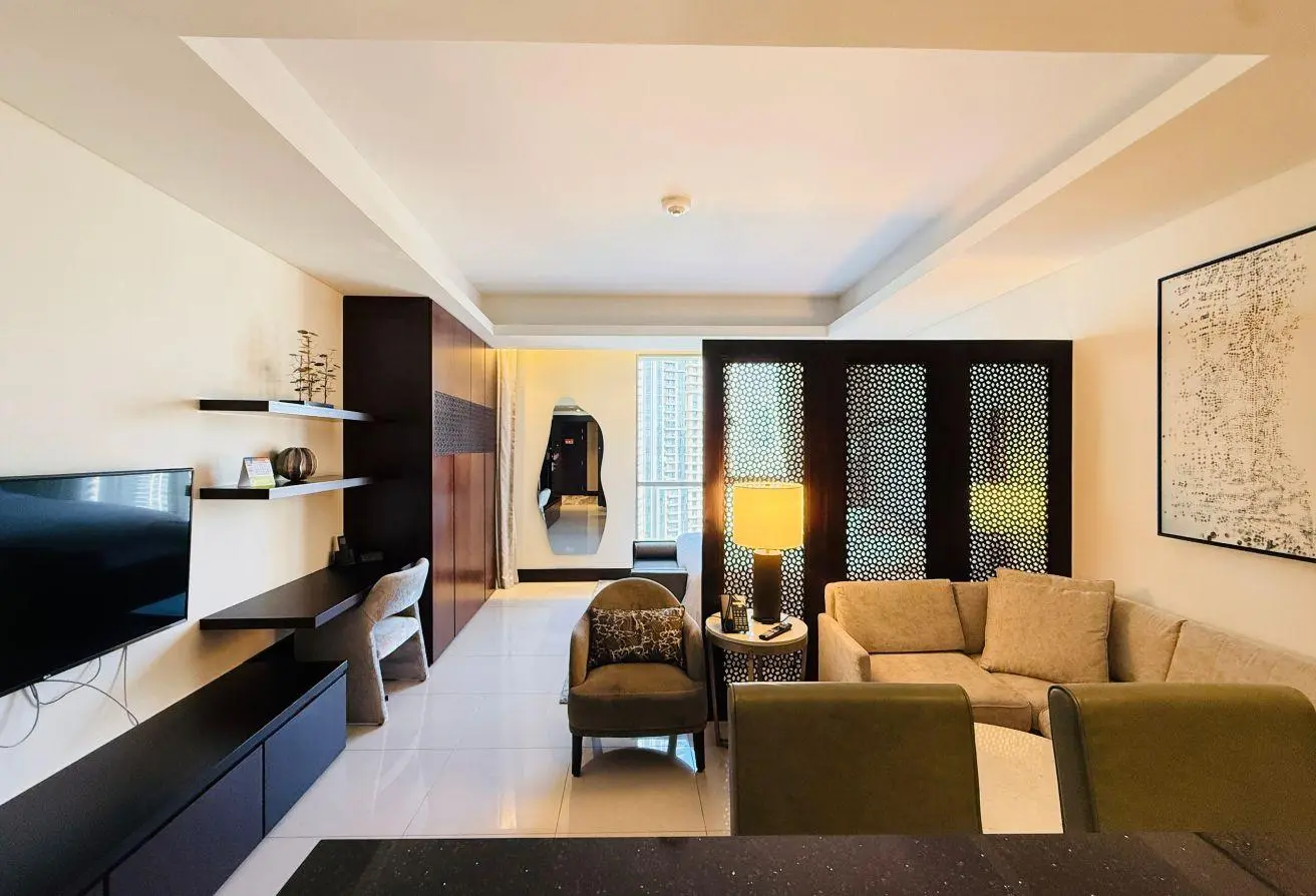 Modern living room with a wall-mounted TV, dark wood shelves, and a beige sofa set, partition panels, and warm lighting.