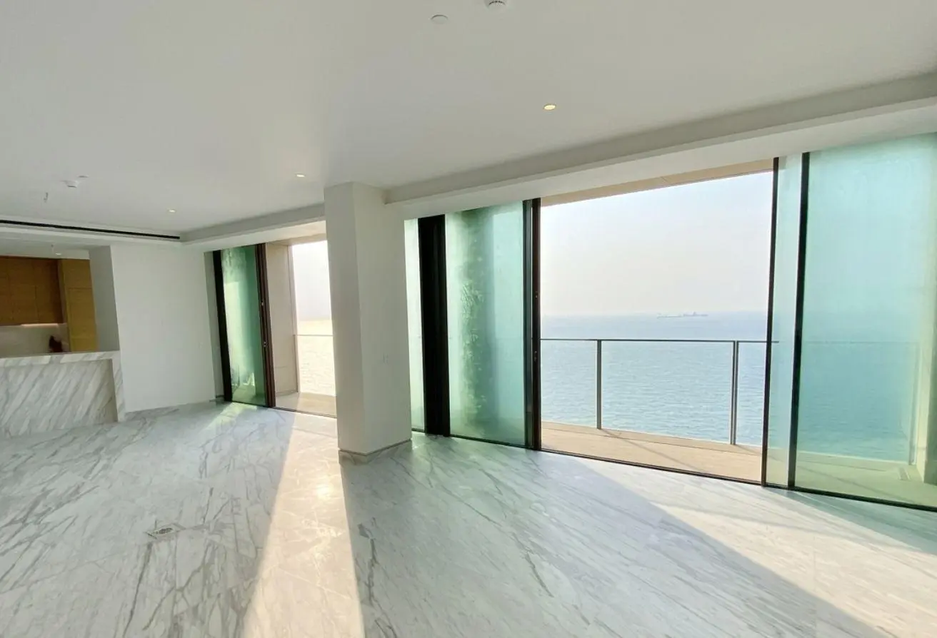 Open-plan living space with white walls, marble flooring, and large sliding glass doors to a balcony with an ocean view.