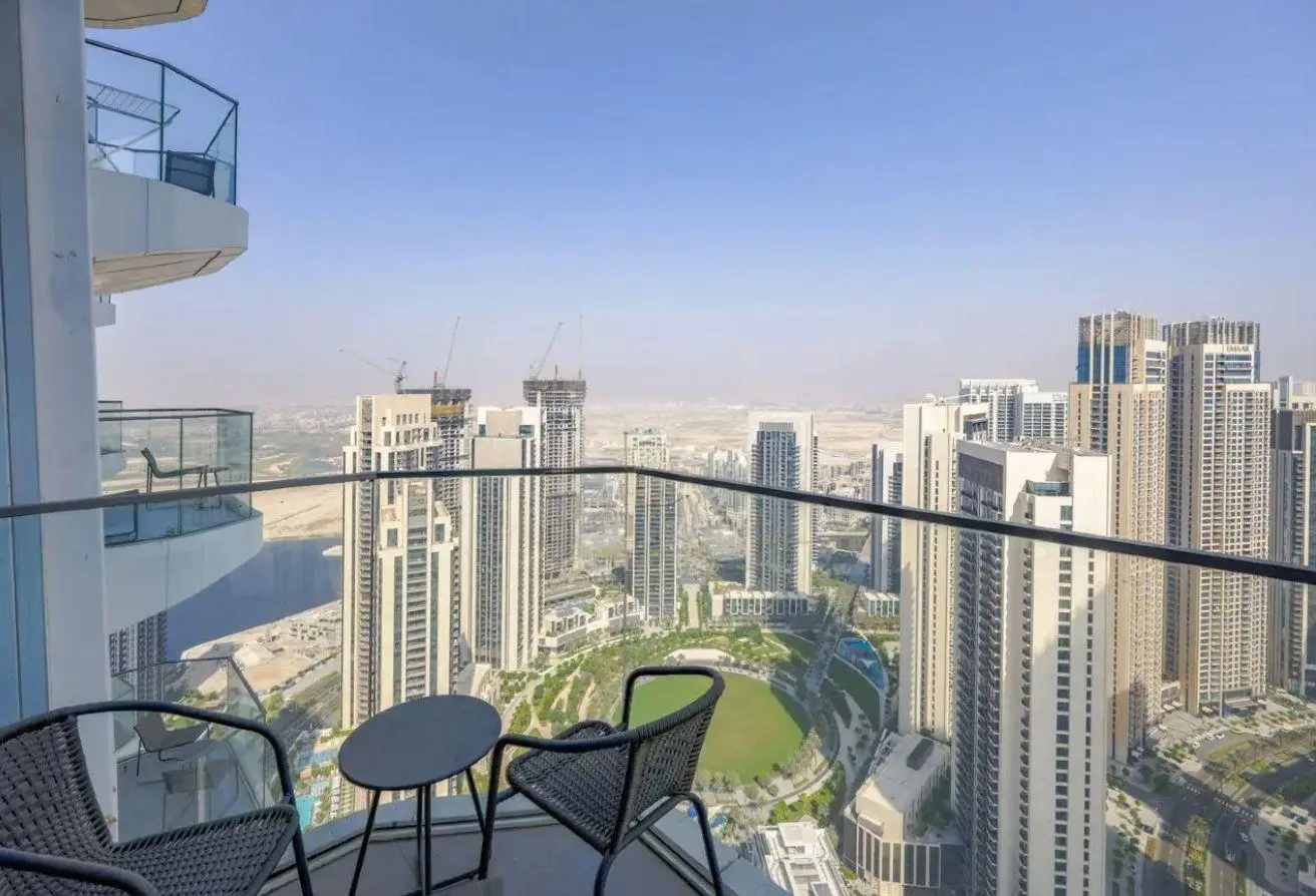 Balcony seating with two chairs and a small round table overlooking a dense city of tall skyscrapers and a circular green park below.