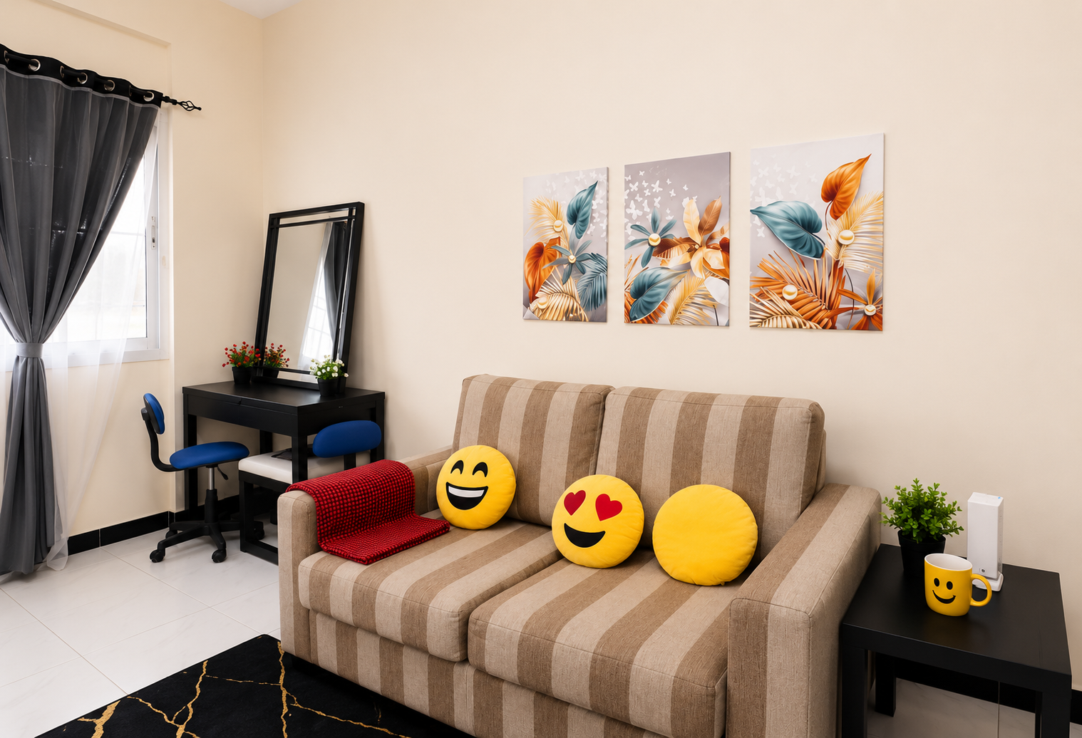 Cozy living room with a beige striped sofa adorned with emoji cushions, a red throw, and a black desk with a mirror by a window.