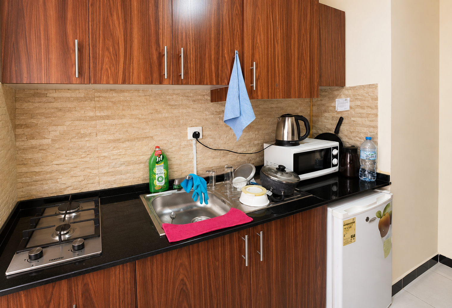Compact kitchen with dark wood cabinets, beige tile backsplash, sink, and small appliances on a black countertop.