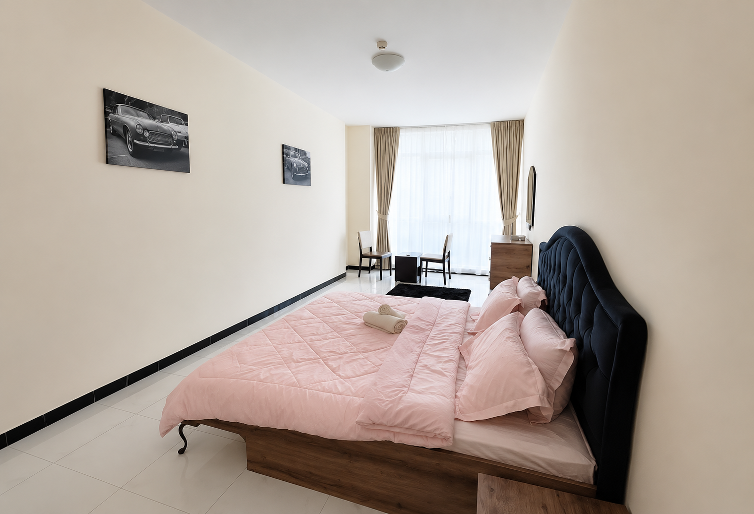 Hotel bedroom with pink duvet, matching pillows, a dark tufted headboard, and a large window with sheer curtains.