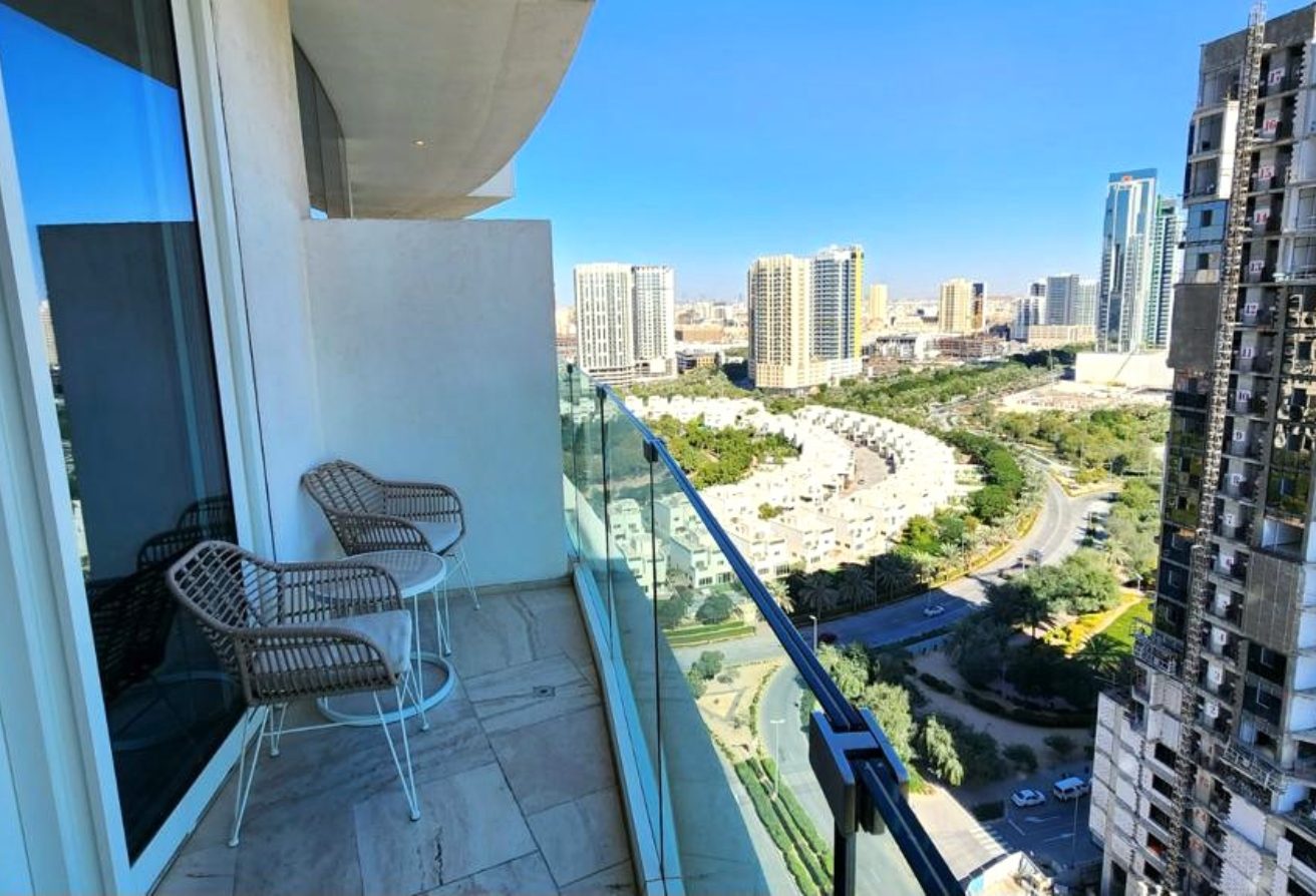 Balcony with two wicker chairs and a small table overlooking a cityscape of high-rise buildings and a curved road.